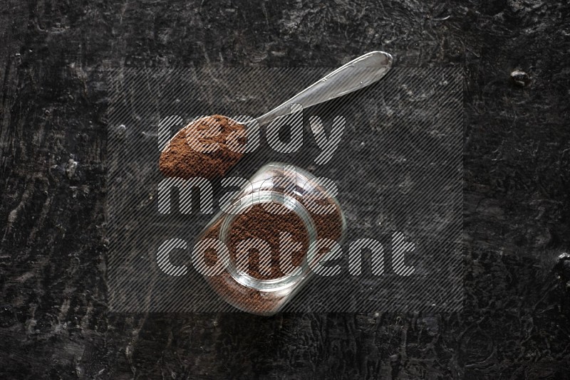 وعاء زجاجي للبهارات وملعقة معدنية ممتلئان ببودرة القرنفل على أرضية سوداء