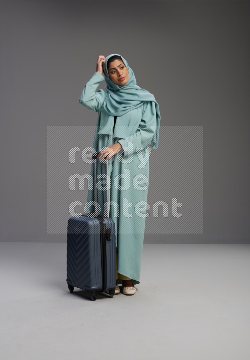 Saudi Woman wearing Abaya standing holding Travel bag on Gray background