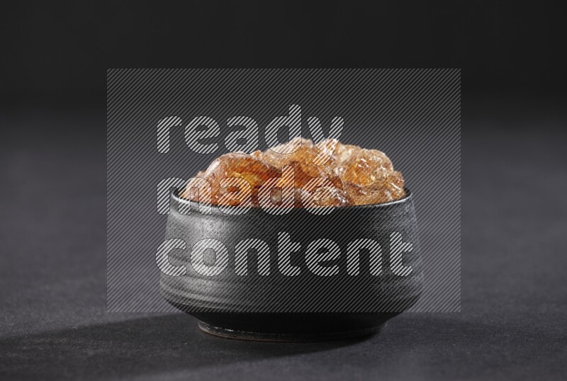 A black pottery bowl full of gum arabic on black flooring