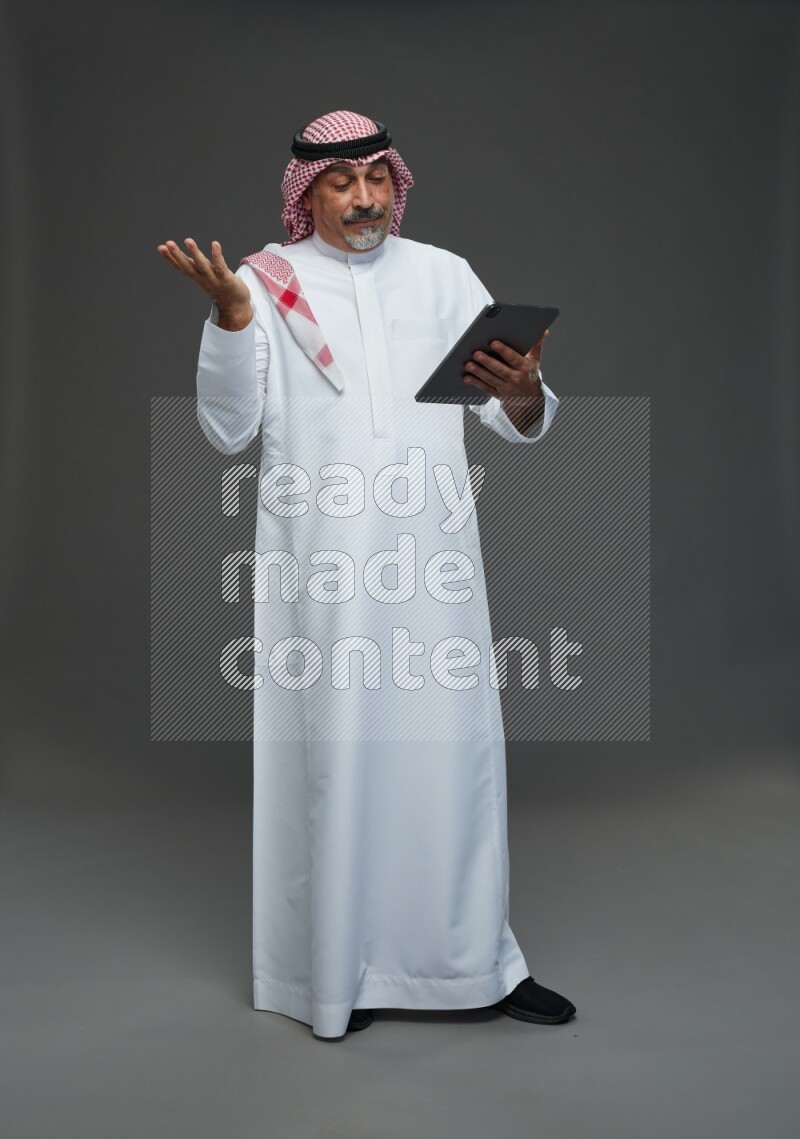 Saudi man with shomag Standing working on tablet on gray background