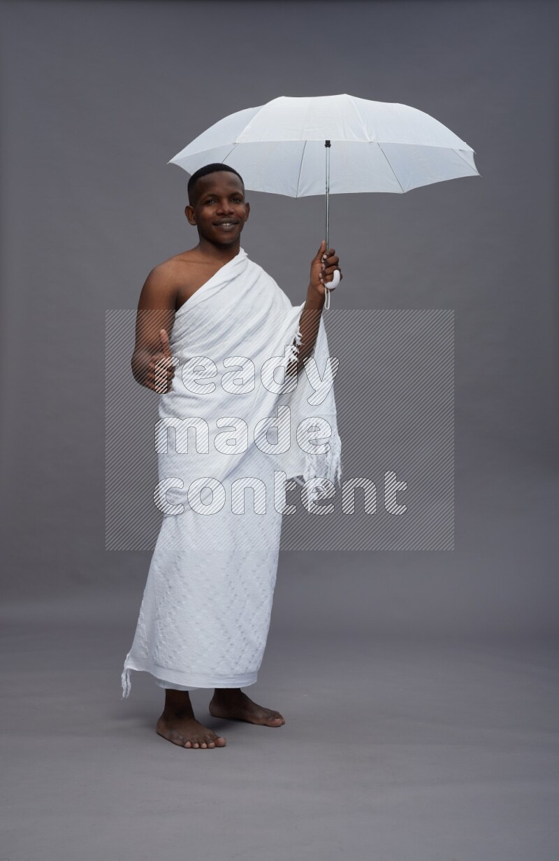 A man wearing Ehram Standing holding umbrella on gray background