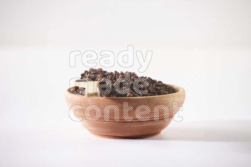 A wooden bowl and a wooden spoon full of cloves on a white flooring