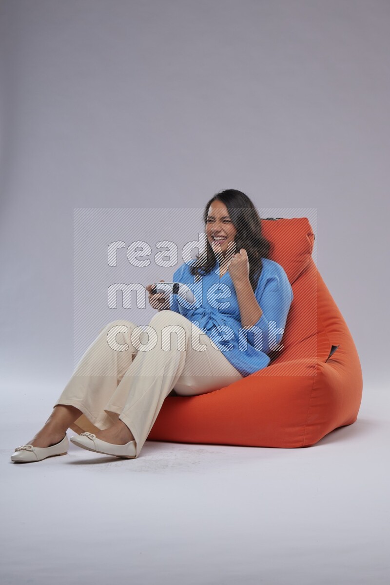A woman sitting on an orange beanbag and gaming with joystick