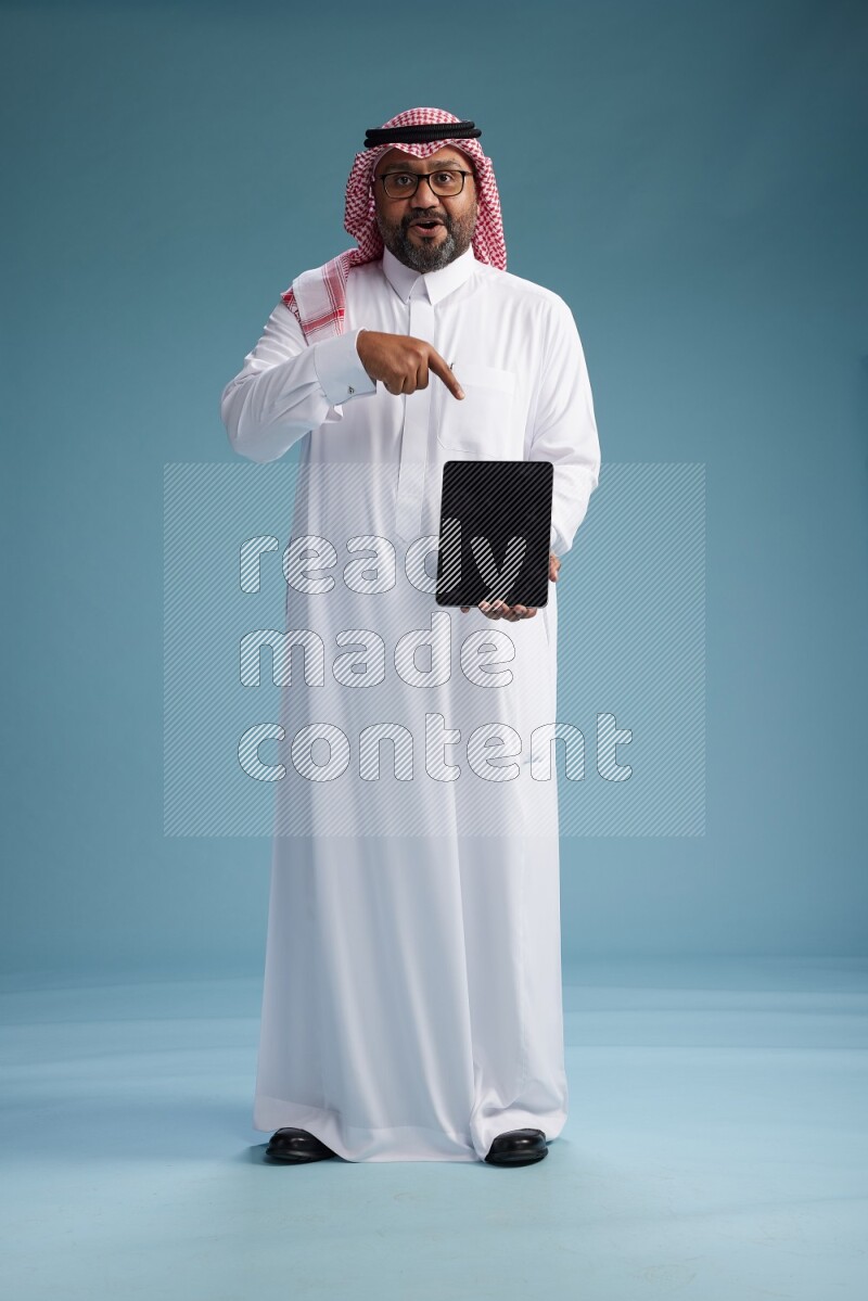 Saudi Man with shimag Standing holding a tablet on blue background