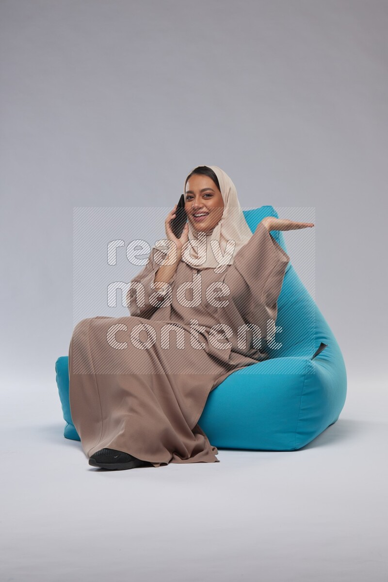 A Saudi woman sitting on a blue beanbag and working on laptop