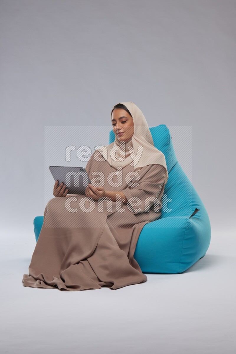 A Saudi woman sitting on a blue beanbag and working on tablet
