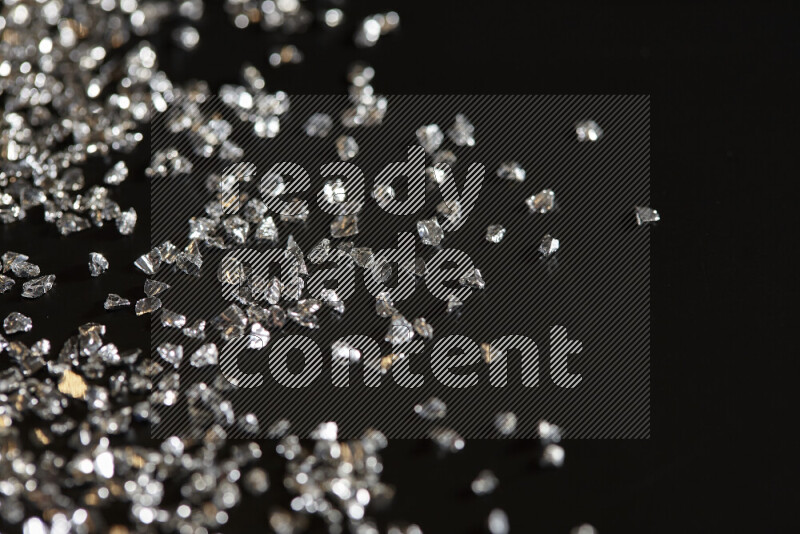 Silver shimmering fragments of glass scattered on a black background