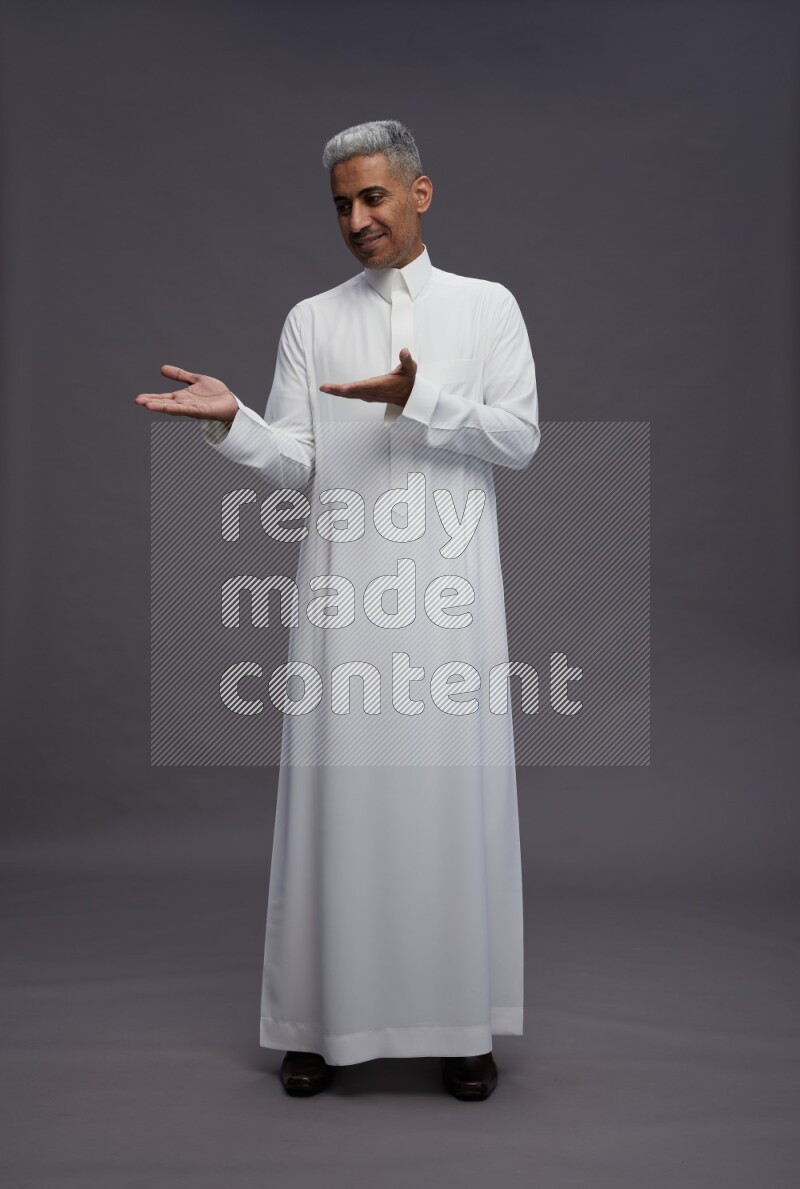 Saudi man wearing thob standing interacting with the camera on gray background