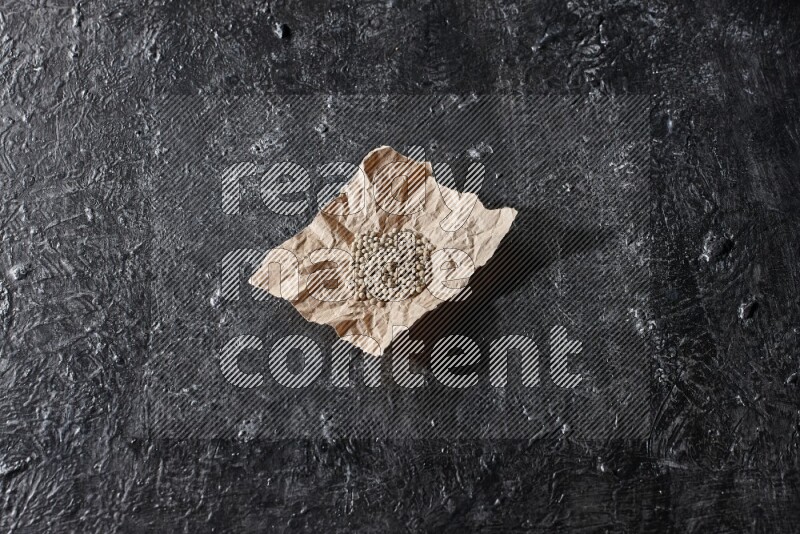 White pepper beads in a crumpled piece of on textured black flooring