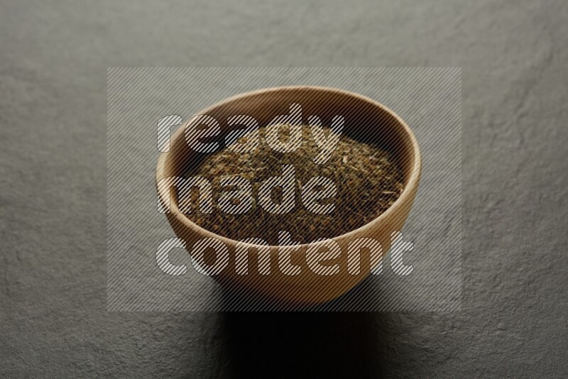 wooden round sauce bowl filled with herbs on grey textured countertop