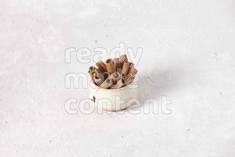 Cinnamon sticks in a beige bowl on a white background