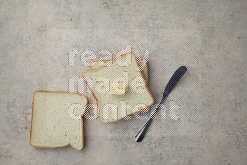 White toast slices with a butter cube and a spreading knife on a light blue textured background