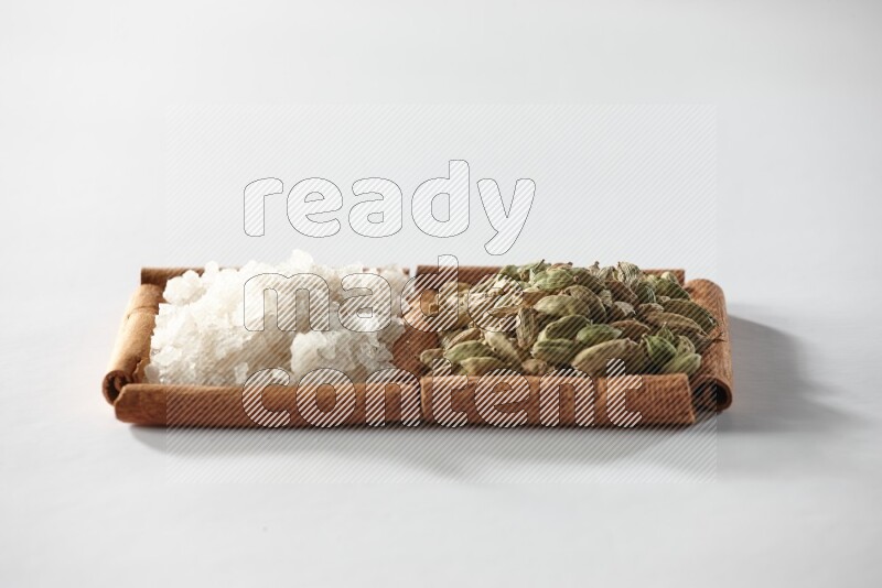 2 squares of cinnamon sticks full of cardamom and white salt on white flooring
