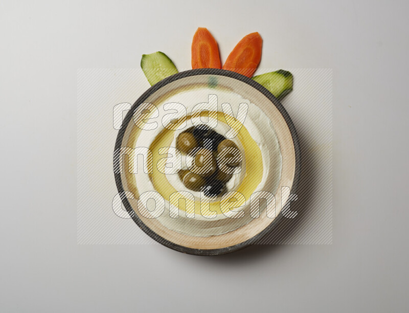 Lebnah garnished with whole black olives in a pottery plate on a white background