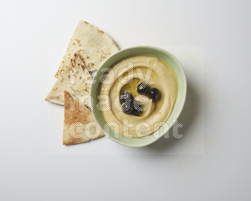 Hummus in a green plate garnished with black olives on a white background