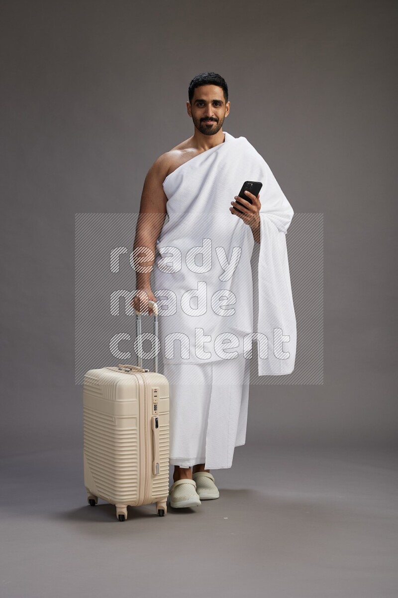 A man wearing Ehram Standing holding traveling bag on gray background