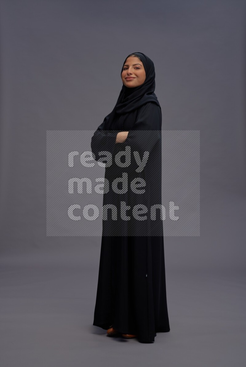 Saudi woman wearing Abaya standing with crossed arms on gray background