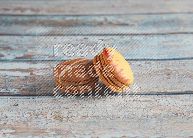 45º Shot of of two assorted Brown Irish Cream, and Orange Exotic macarons on light blue background