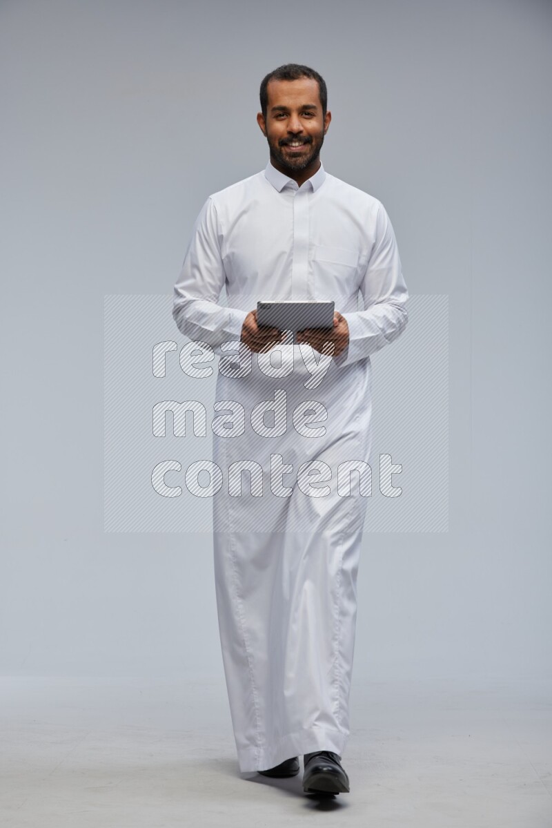 Saudi man wearing Thob standing working on tablet on Gray background