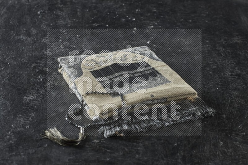 سجادة صلاة مطوية بعناصر مختلفة مثل القرآن الكريم وسبحة الصلاة على خلفية سوداء