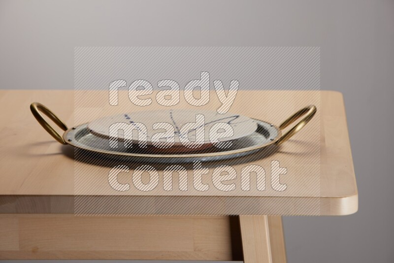 multicolored plate placed on a rounded stainless steel tray with golden handels on the edge of wooden table