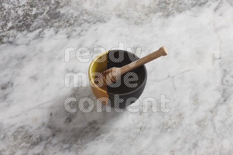 Multicolored pottery bowl with wooden honey dipper in it on grey marble background