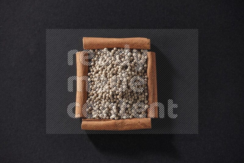 A single square of cinnamon sticks full of white pepper on black flooring