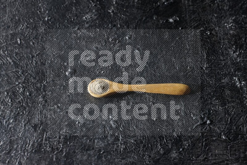 ملعقة خشبية مليئة ببودرة الفلفل الأبيض على أرضية سوداء