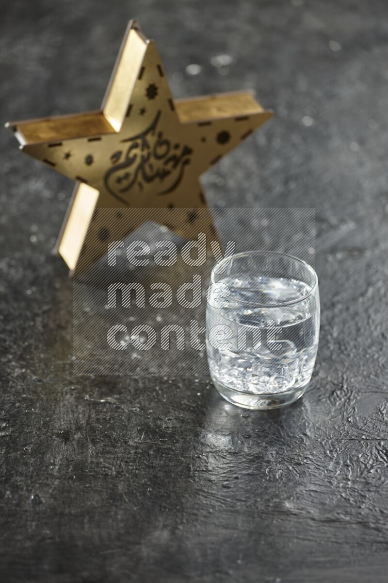 A wooden golden star lantern with different drinks, dates, nuts, prayer beads and quran on textured black background