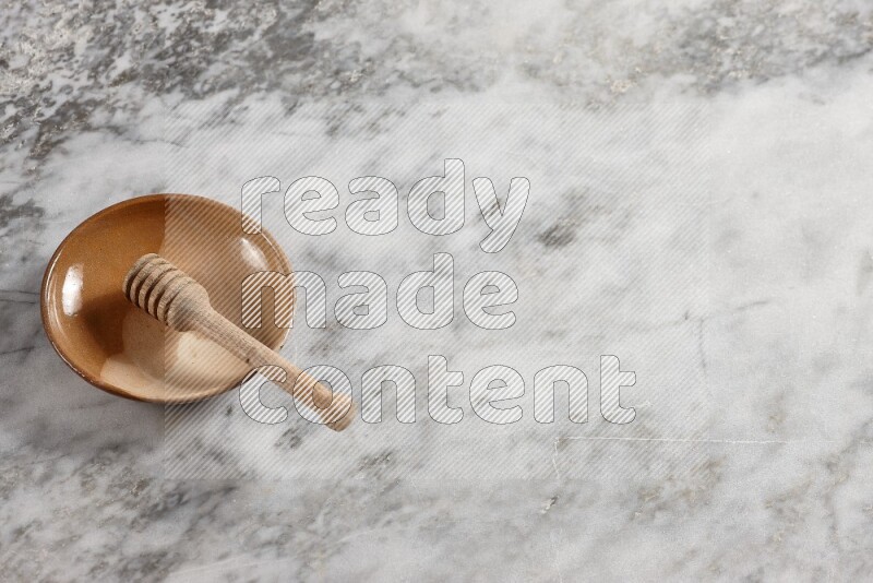 Multicolored pottery plate with wooden honey dipper in it on grey marble background