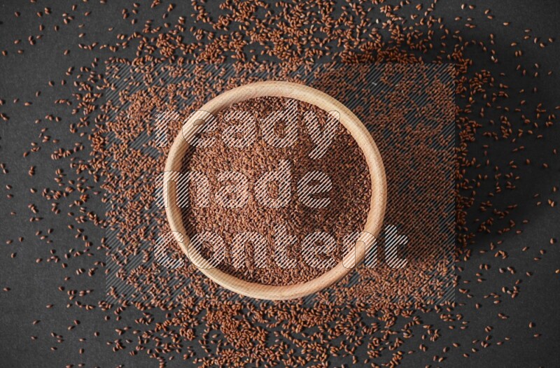 A wooden bowl full of garden cress seeds surrounded by seeds on a black flooring
