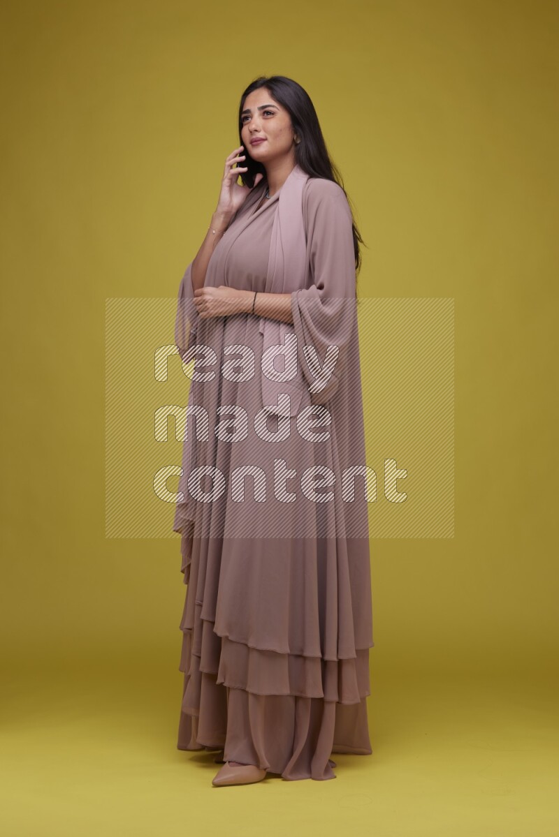 A woman Calling on a Yellow Background wearing Brown Abaya