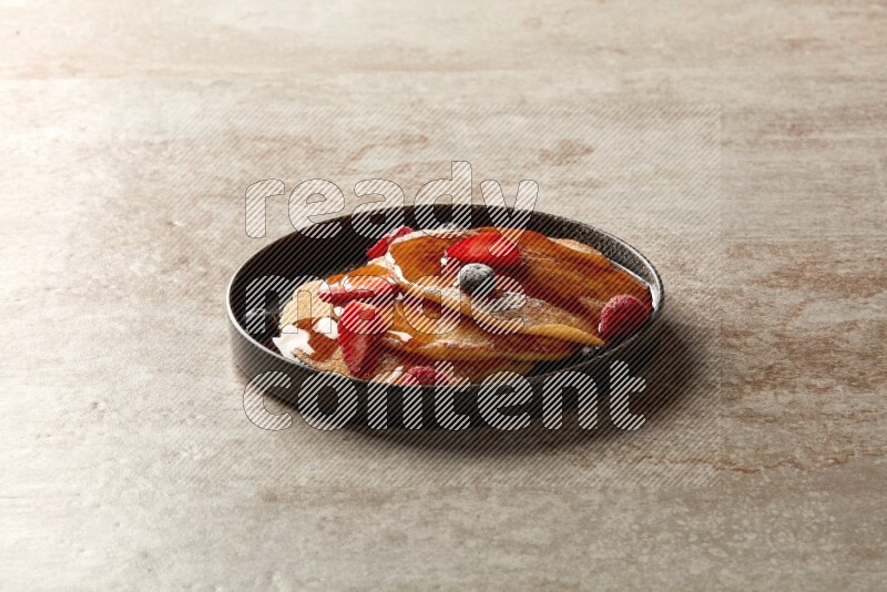 Three stacked mixed berries pancakes in a black plate on beige background