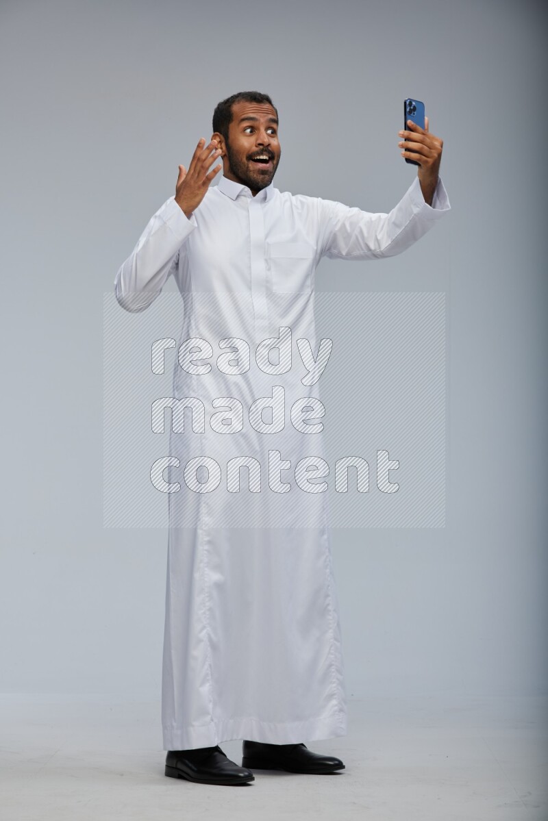 Saudi man wearing Thob standing taking selfie on Gray background