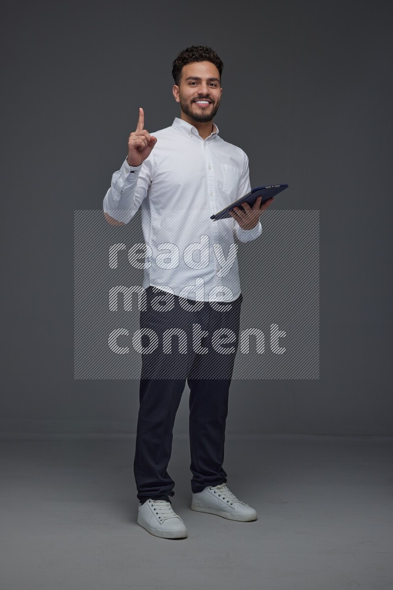 A man wearing smart casual standing and using his tablet and making multi hand gestures eye level on a gray background