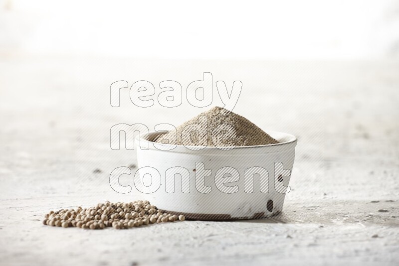 white pottery bowl full of white pepper powder with pepper beads on textured white flooring