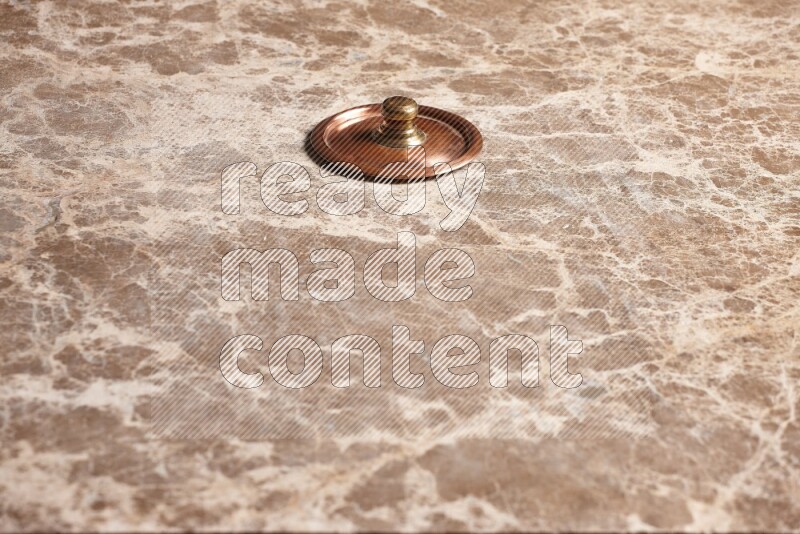 A small copper pot lid on beige marble background