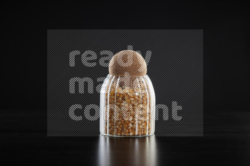 Dry corn kernels in a glass jar on black background