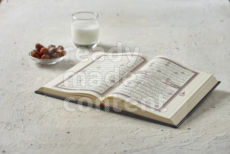 Quran with dates, prayer beads and different drinks all placed on textured white background