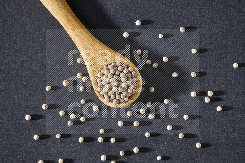 A wooden spoon full of white pepper beads on black flooring