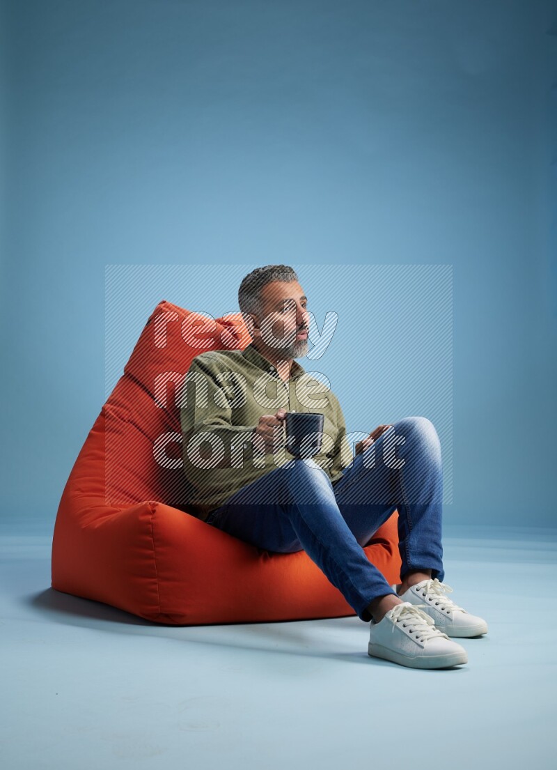 A man sitting on an orange beanbag and drinking coffee