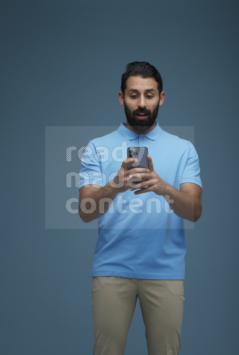 A man Texting on his phone in a blue background wearing a Blue shirt