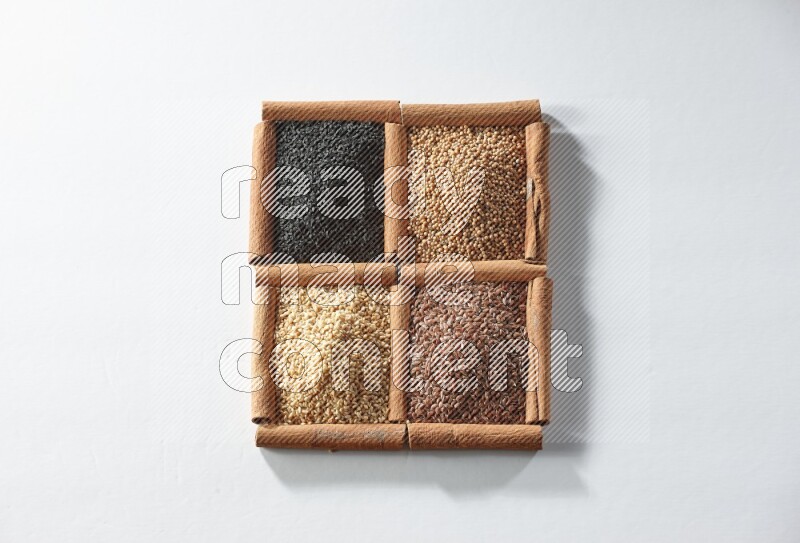 4 مربعات من أعواد القرفة ممتلئة بحبة البركة وبذور الخردل وبذور الكتان والسمسم على أرضية بيضاء