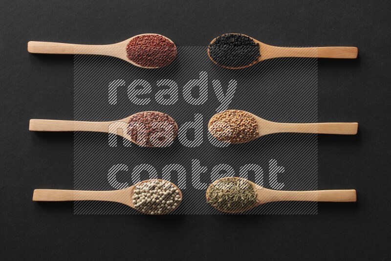 wooden spoons filled with white peppers, mustard seeds, black seeds, garden cress, cumin and flax on black flooring