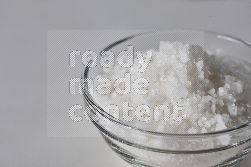 A glass bowl full of coarse sea salt crystals on white background