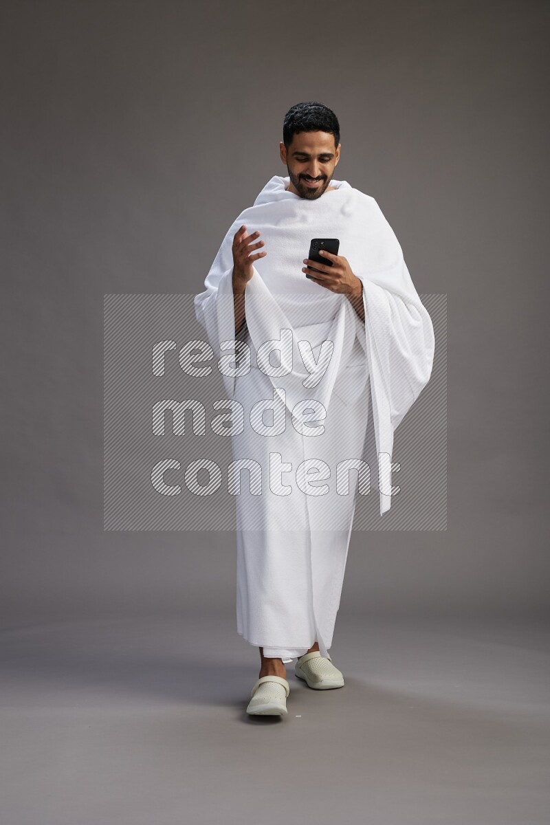 A man wearing Ehram Standing texting on phone on gray background