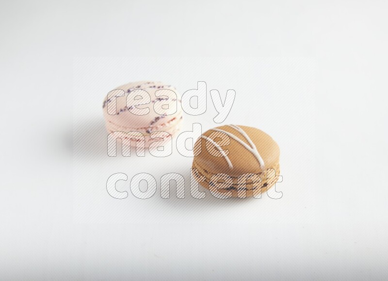 45º Shot of of two assorted Brown Irish Cream, and pink orange blossom macarons on white background