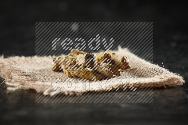 أصابع الكركم المجففة على قطعة من قماش الخيش على خلفية سوداء