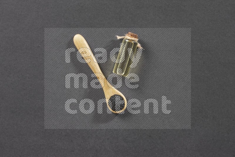 ملعقة خشبية ممتلئة بحبة البركة مع زجاجة من زيت حبة البركة على أرضية سوداء