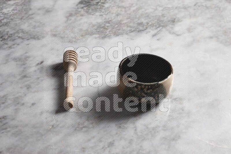 Multicolored pottery bowl with wooden honey dipper on the side on grey marble background
